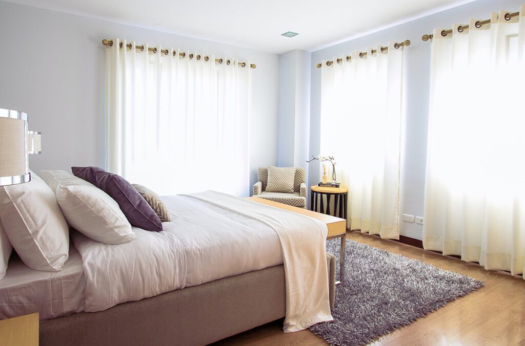 A vacation rental bedroom with purple bedding, and bright windows.