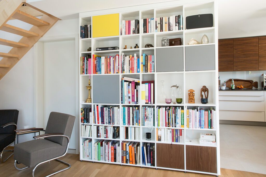 A cubby style book case is used as a room divider in a living room to kitchen space