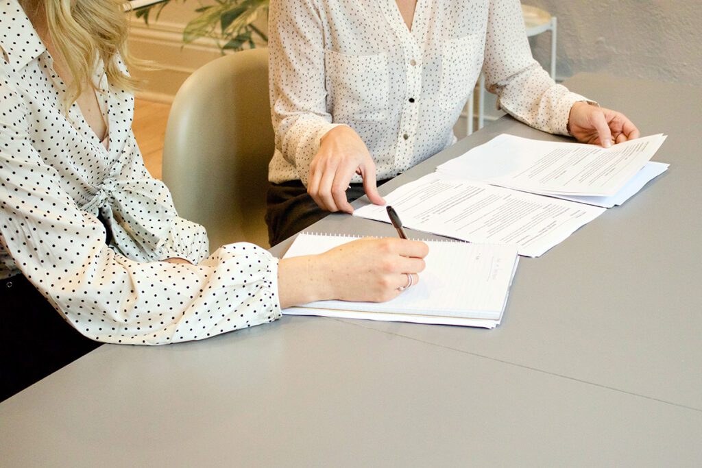 Two women sit at a table with zoning and permit paperwork for their rental property.